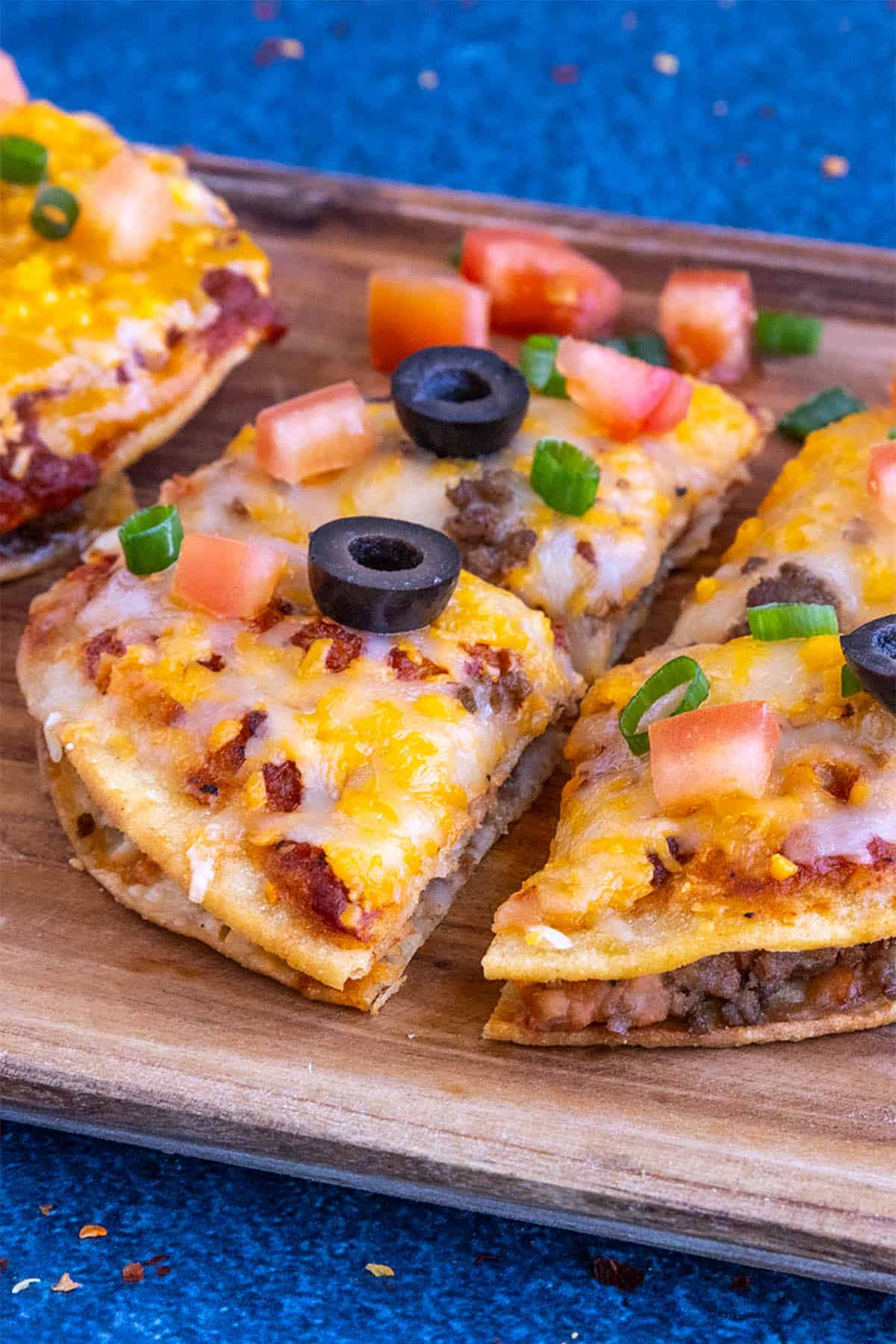 Close-up of a Taco Bell-style Mexican Pizza sliced into 4 pieces, garnished with chopped tomato, black olives, and green onion