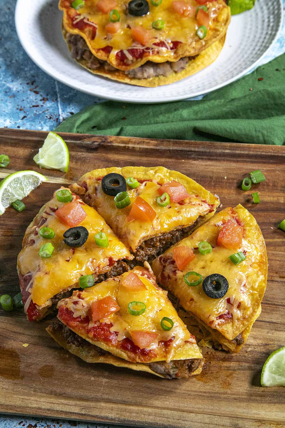 A Taco Bell-style Mexican Pizza on a serving tray, sliced into 4 pieces, garnished with chopped tomato, black olives, and green onion