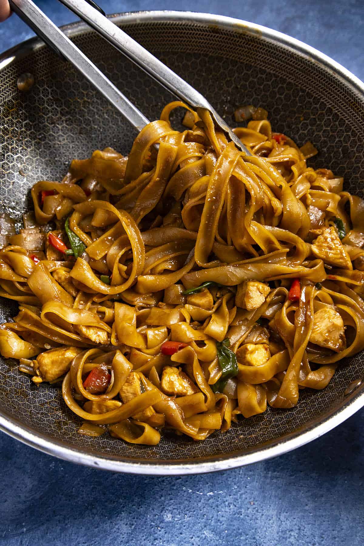 Serving Drunken Noodles from the wok with tongs