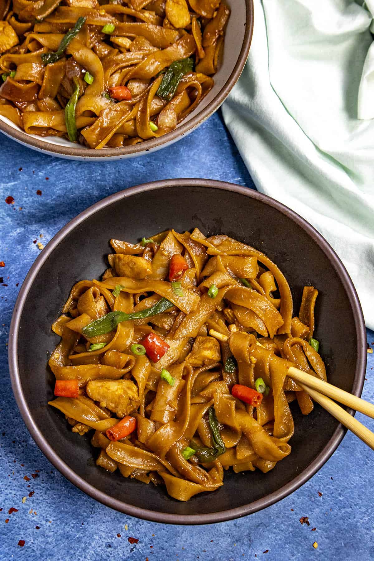 Saucy Drunken Noodles served up in a dark bowl, with chopsticks to enjoy