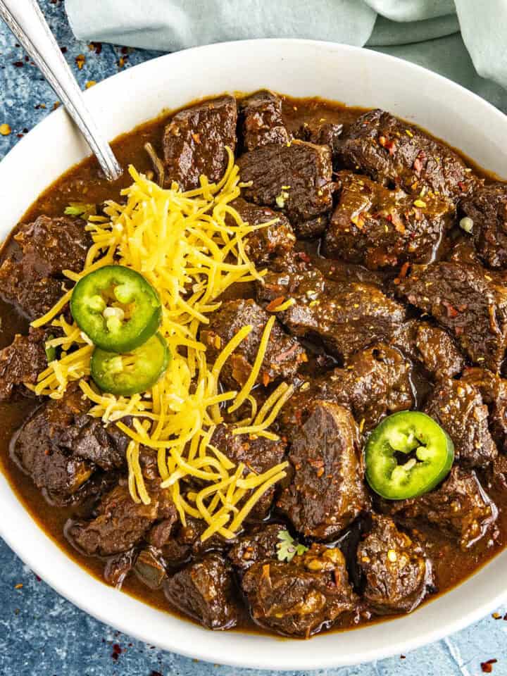 A meaty bowl of Texas Chili served with shredded cheese and sliced chilies on top