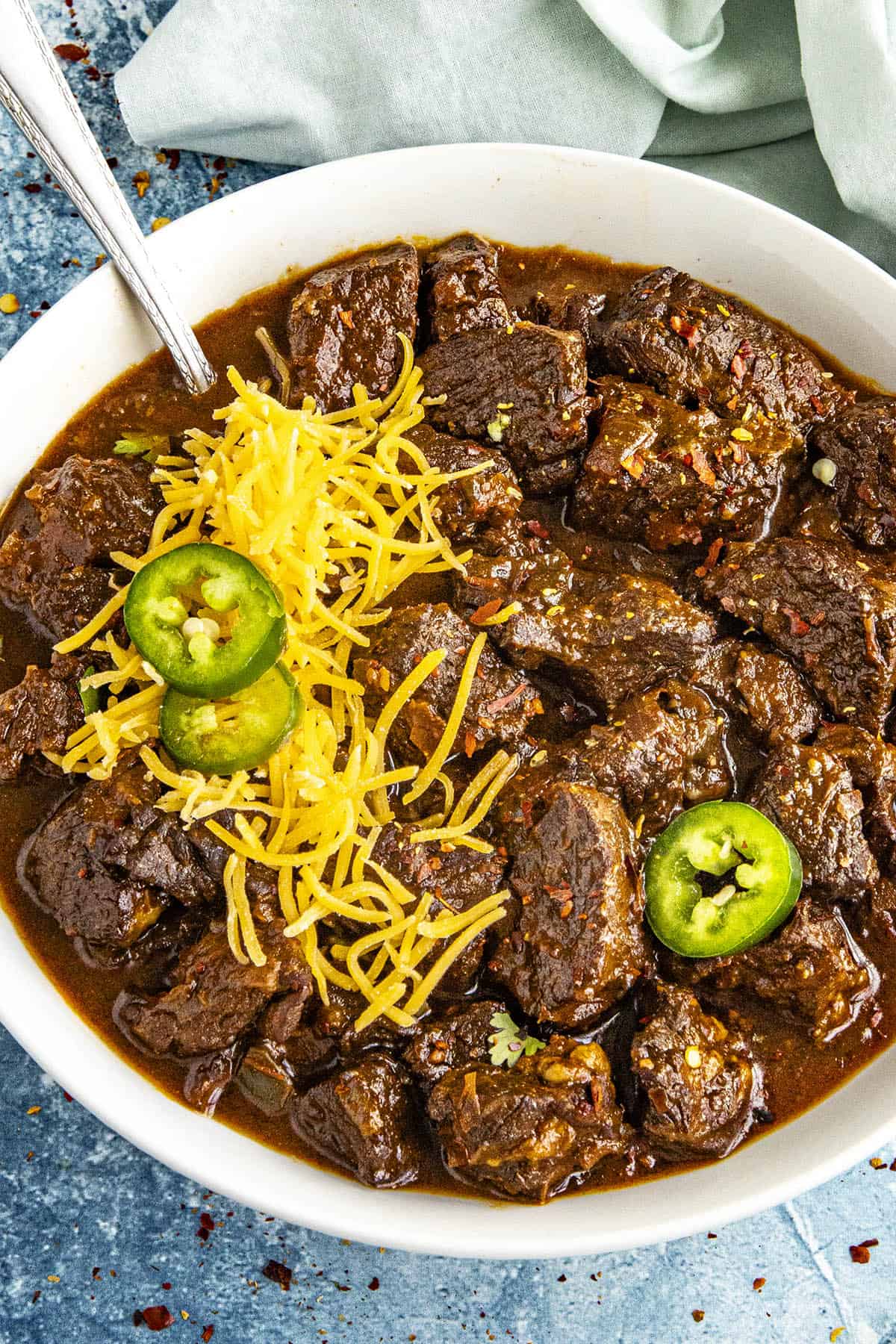 A meaty bowl of Texas Chili served with shredded cheese and sliced chilies on top