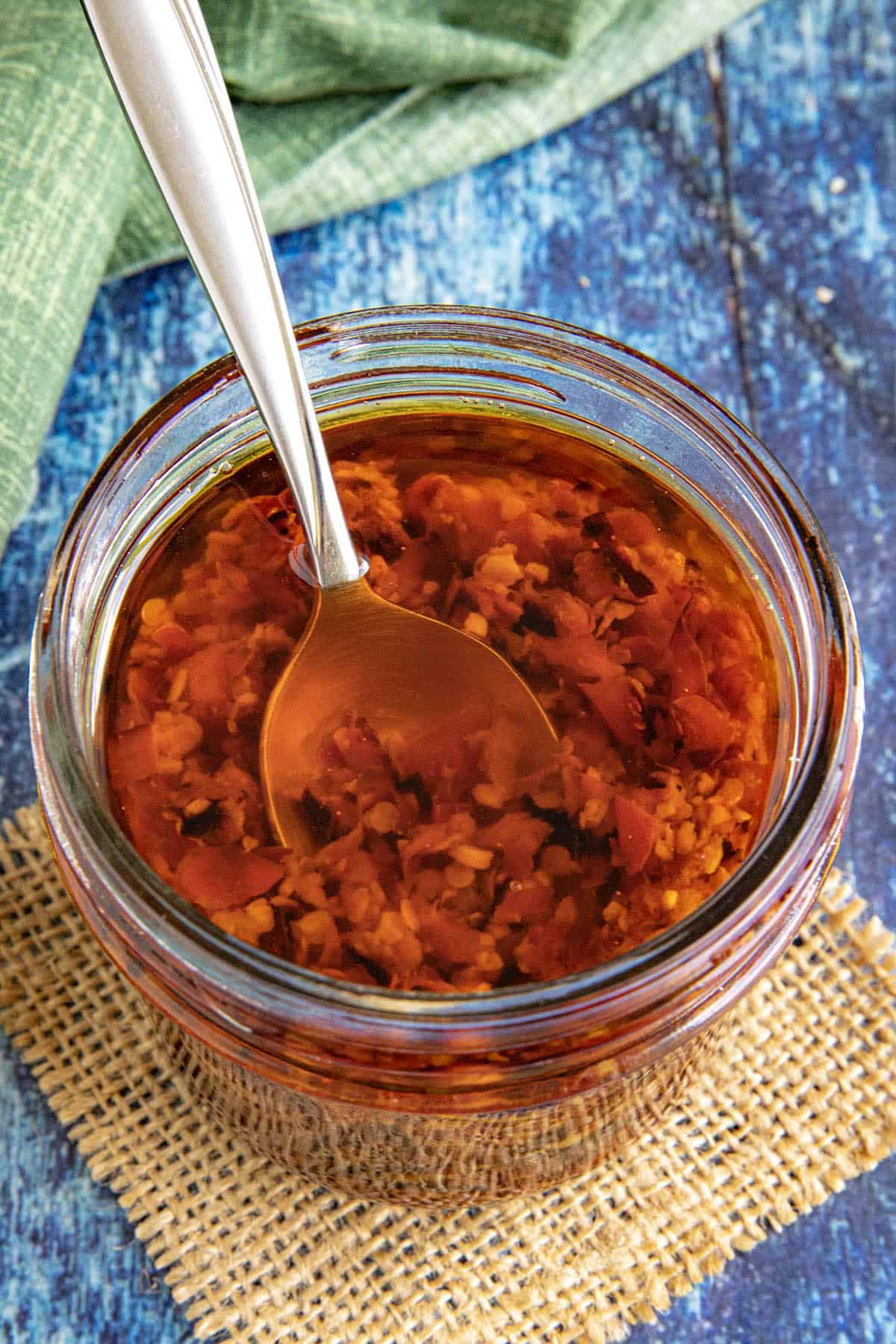 A jar full of Serrano-Garlic Chili Crunch with a serving spoon