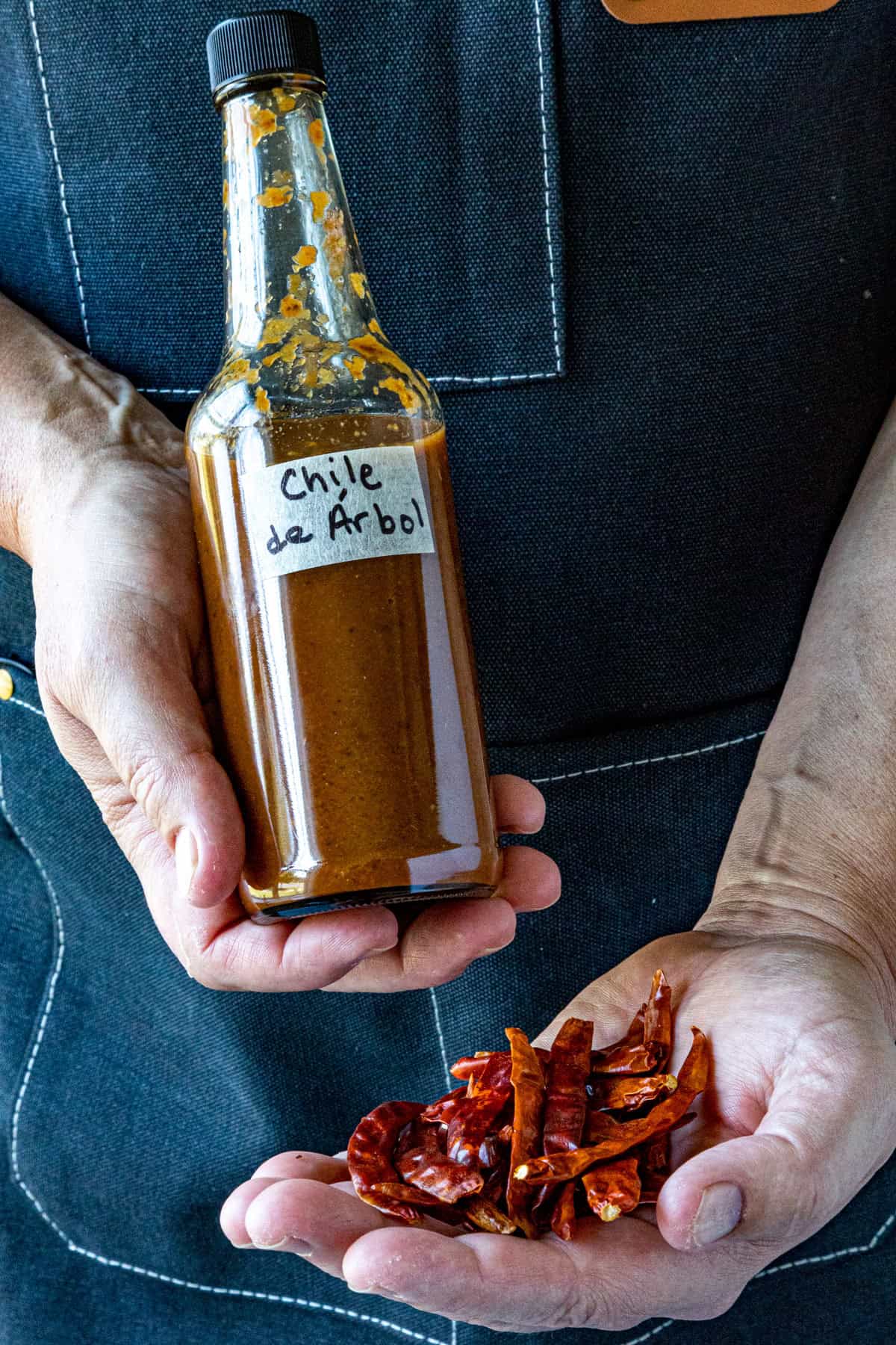 Mike holding a bottle of Chili de &Aacute;rbol Hot Sauce and dried chiles de arbol