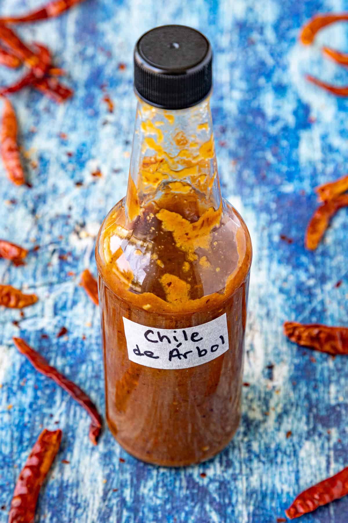 A bottle of fiery Chili de &Aacute;rbol Hot Sauce surrounded by dried chilies