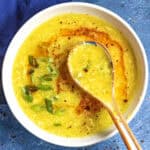 Freshly made Chinese egg drop soup in a bowl with a spoon, topped with spicy chili oil