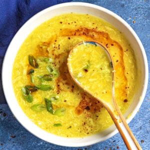 Freshly made Chinese egg drop soup in a bowl with a spoon, topped with spicy chili oil
