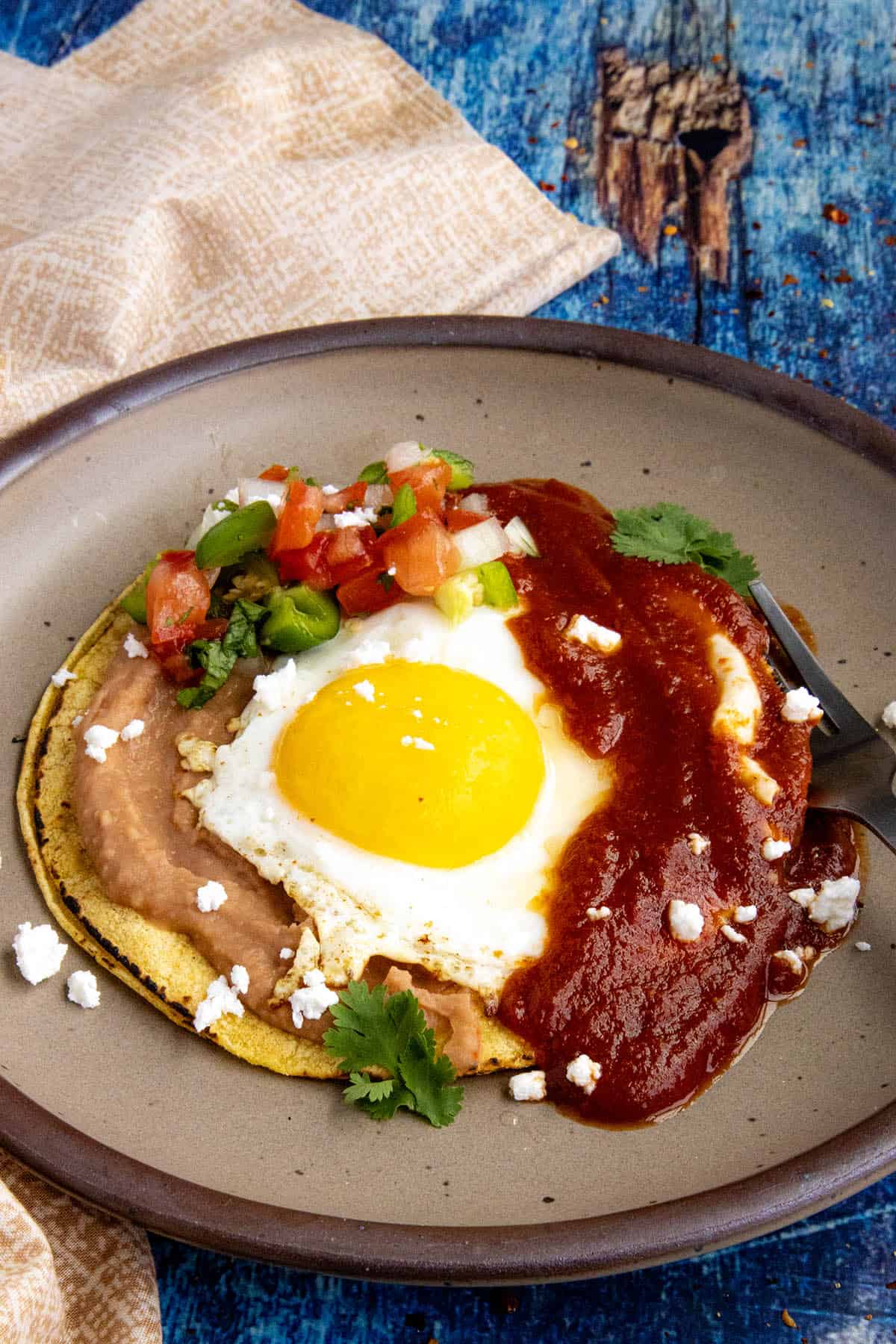 Mexican Huevos Rancheros on a plate, with a sunny-side-up egg served over tortillas with refried beans and ranchero sauce