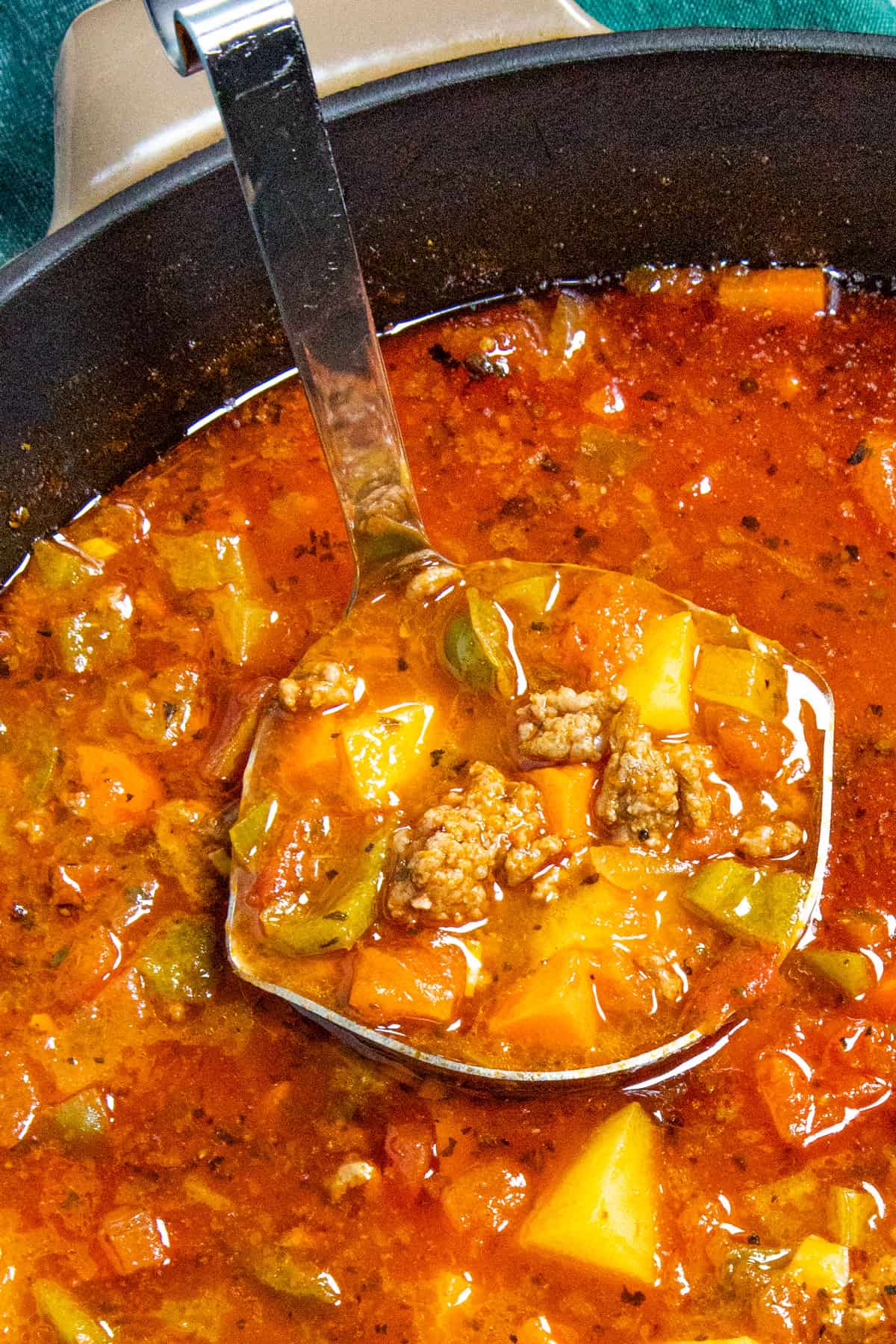 A ladle full of chunky hamburger soup served from the pot