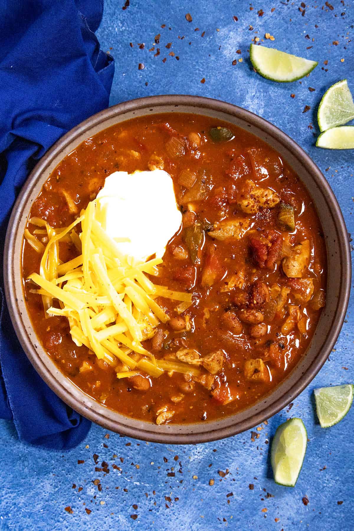 A bowl filled with chunky homemade chicken chili, served with garnish and lime wedges