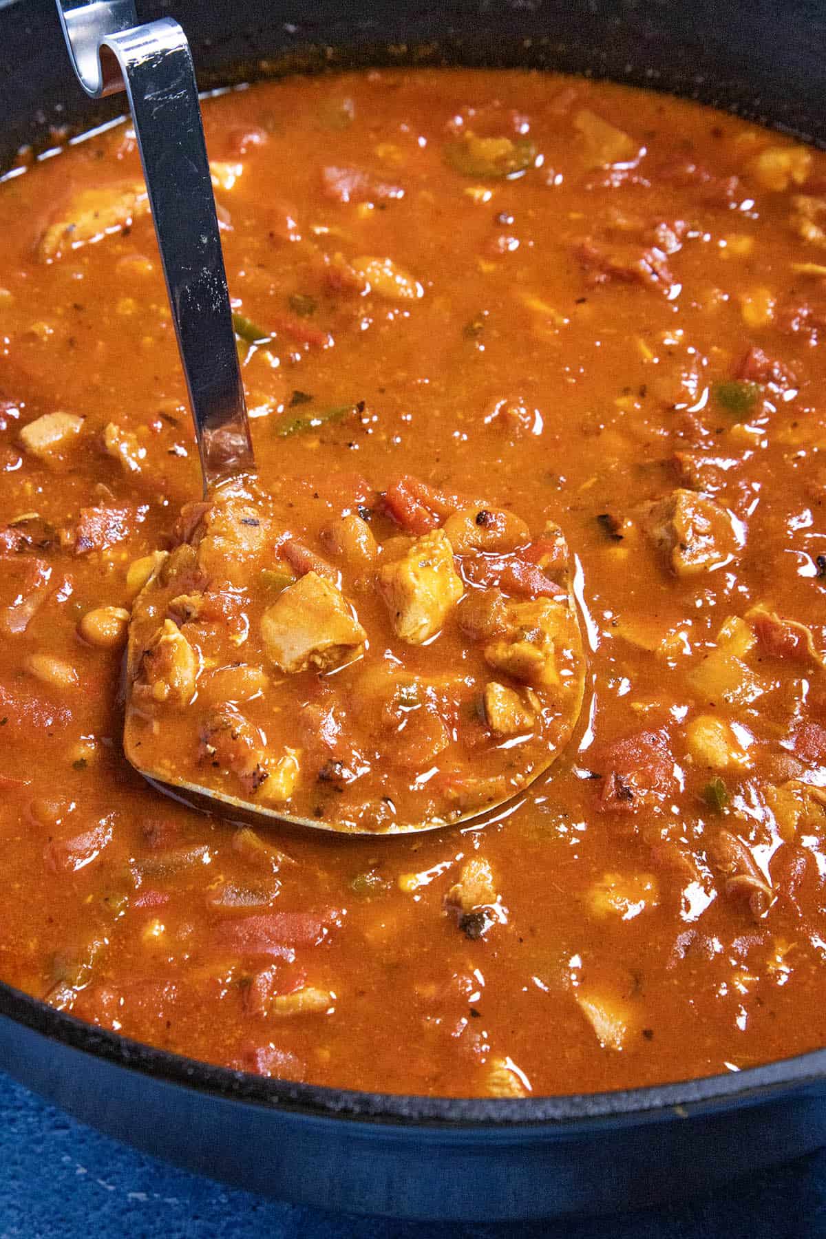 Serving a large spoonful of chunky homemade chicken chili from the pot