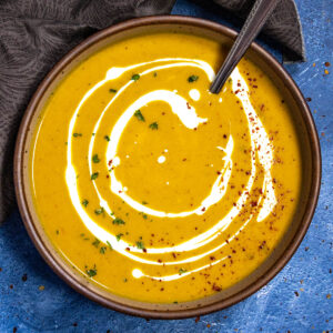 Curried Butternut Squash Soup served in a bowl, garnished with a cream swirl, fresh cilantro, and chili flakes
