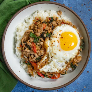 Pad Kra Pao (Thai Basil Stir Fry) in a bowl over rice, topped with a crispy fried egg